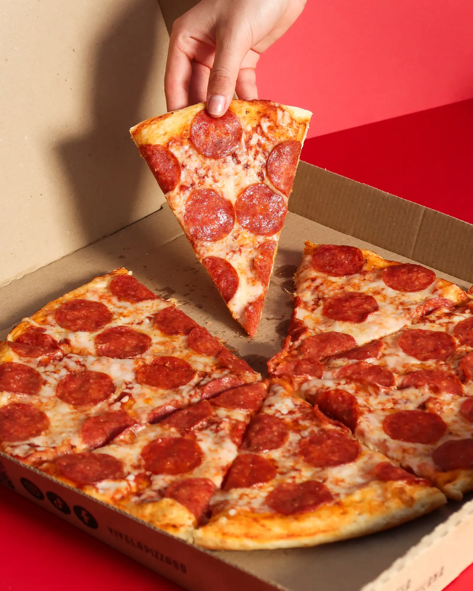 Mano levantando una rebanada de una pizza de pepperoni en su caja Vivela Pizza